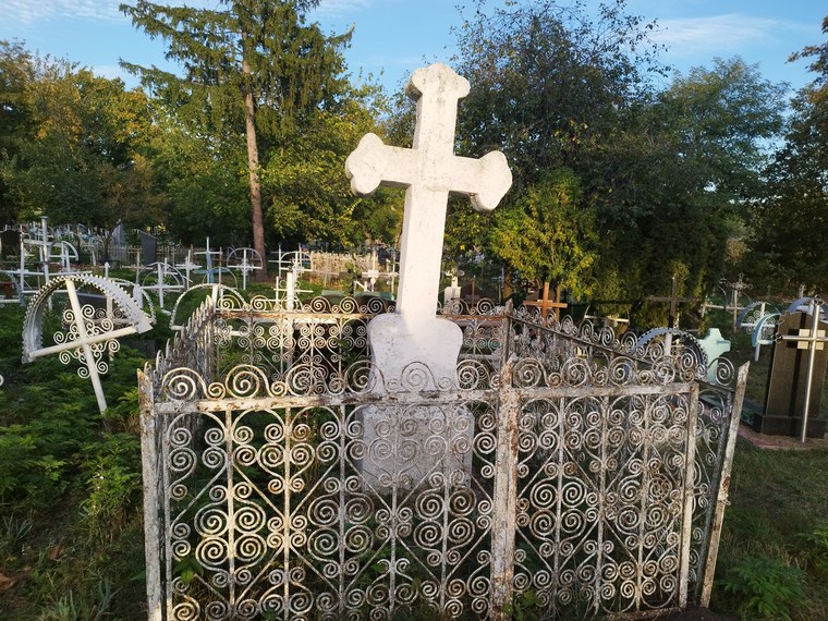 Crucea de piatră din cimitir, în împrejmuirea ei de fier forjat