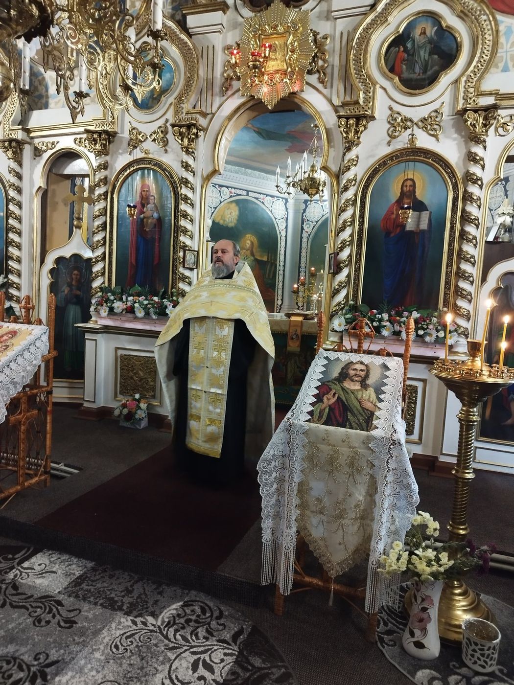 Părintele, în veșminte albe cu aur, în fața iconostasului