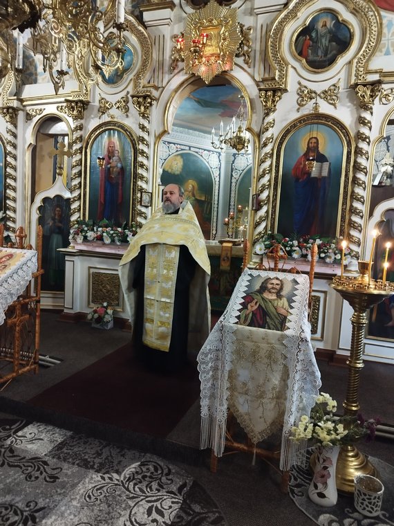 Părintele, în veșminte albe cu aur, în fața iconostasului