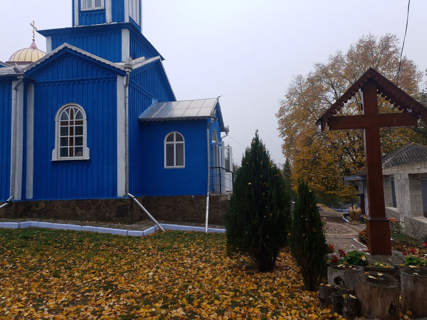 Biserica și crucea mare de lemn din ogradă