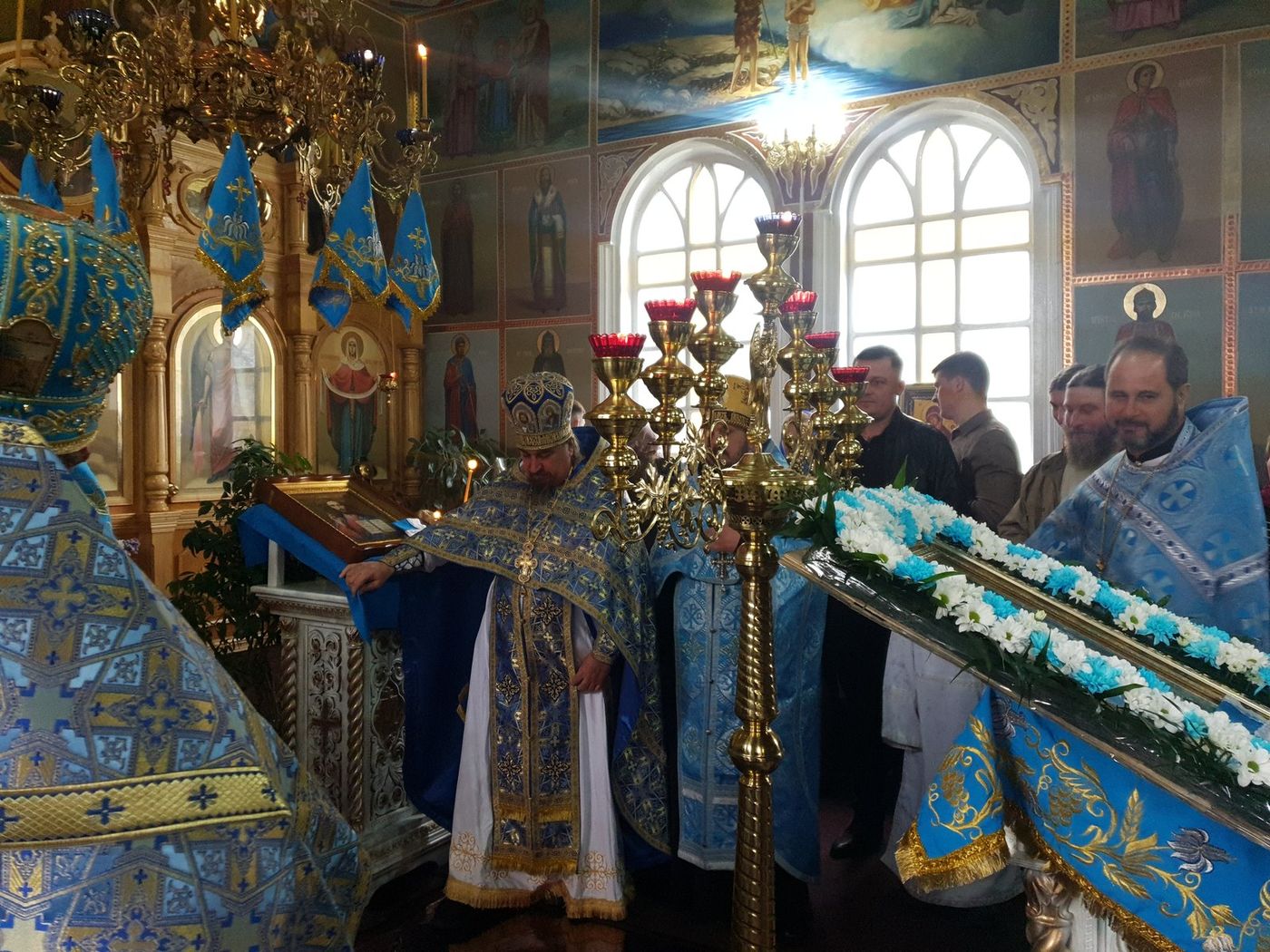 Preoții lângă icoana praznicului, cu credincioșii în spate